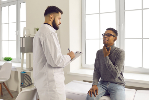 A patient sitting on an exam table explaining his throat cancer symptoms to his doctor