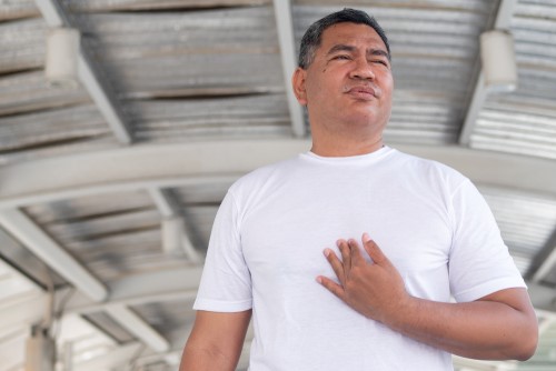 Man in white shirt gripping his chest after experiencing GERD symptoms