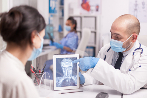 A masked doctor showing a brain scan to a woman with a traumatic brain injury (TBI)