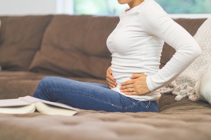 Seated woman feeling her stomach while experiencing pelvic pain