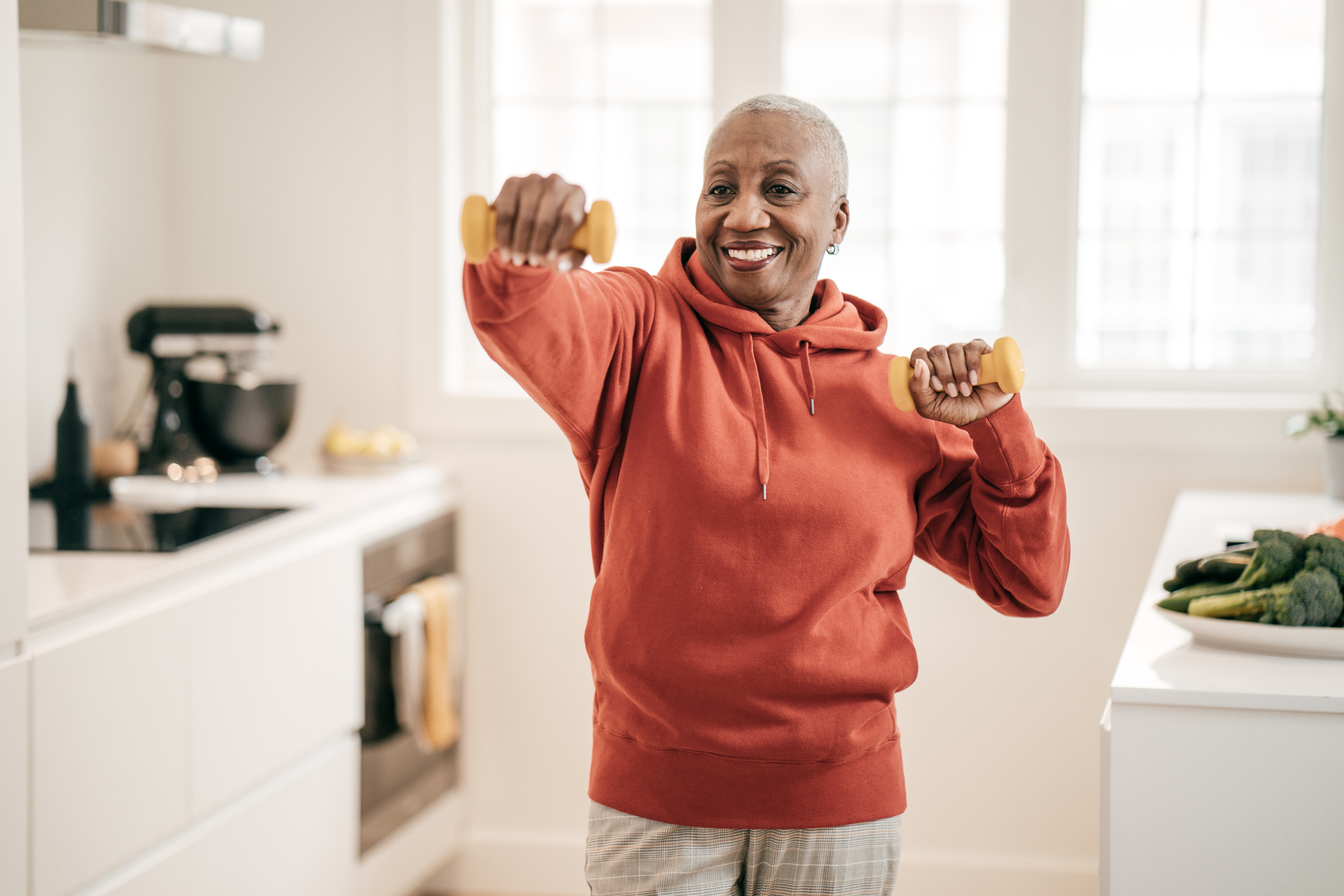 Woman wearing red hoodie working out with yellow hand weights to help combat metabolic syndrome
