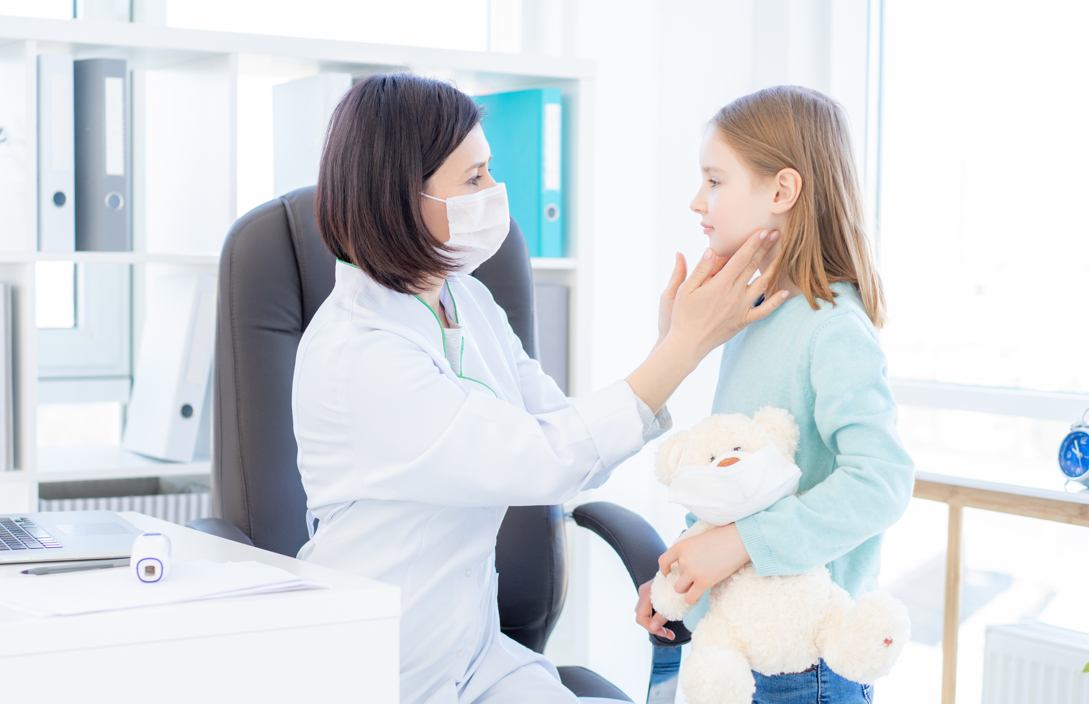 Masked doctor examining a young patient for infectious mononucleosis symptoms through swollen lymph nodes