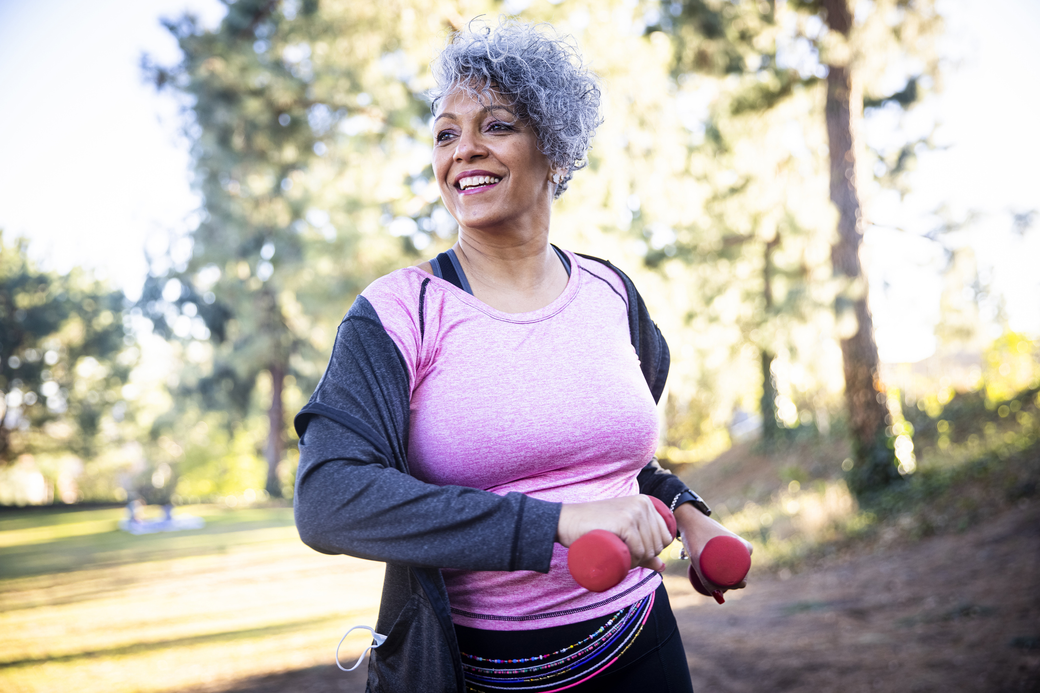 woman in pink shirt exercising with red dumbbells outside after an annual wellness visit