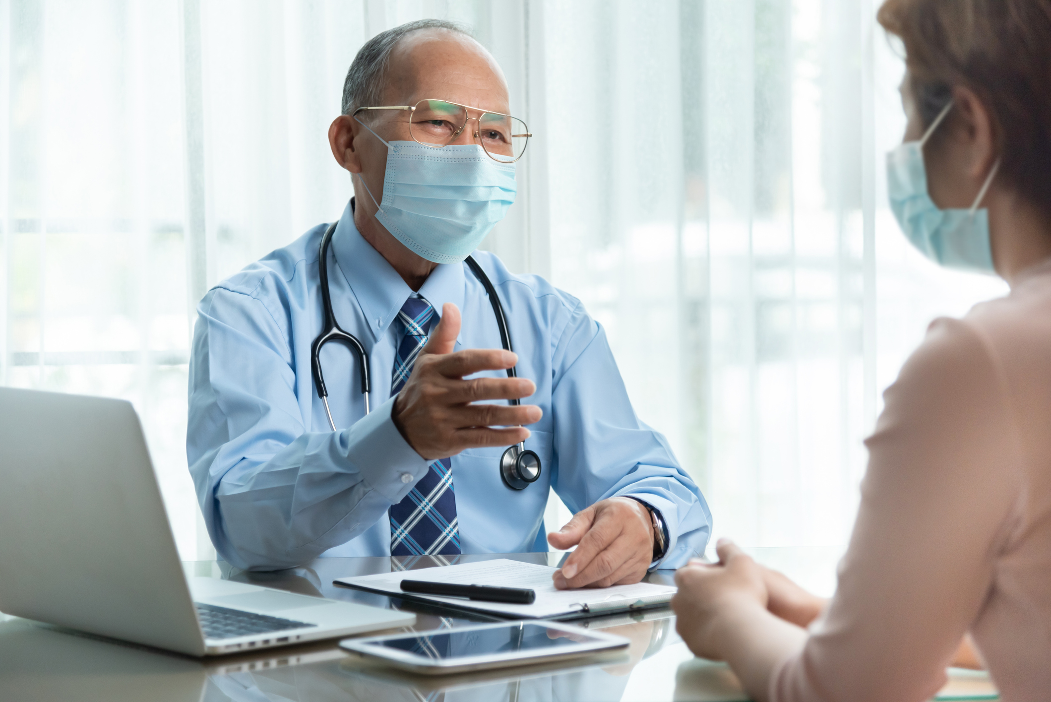 Masked doctor explaining Medicare AWV to a patient across the table