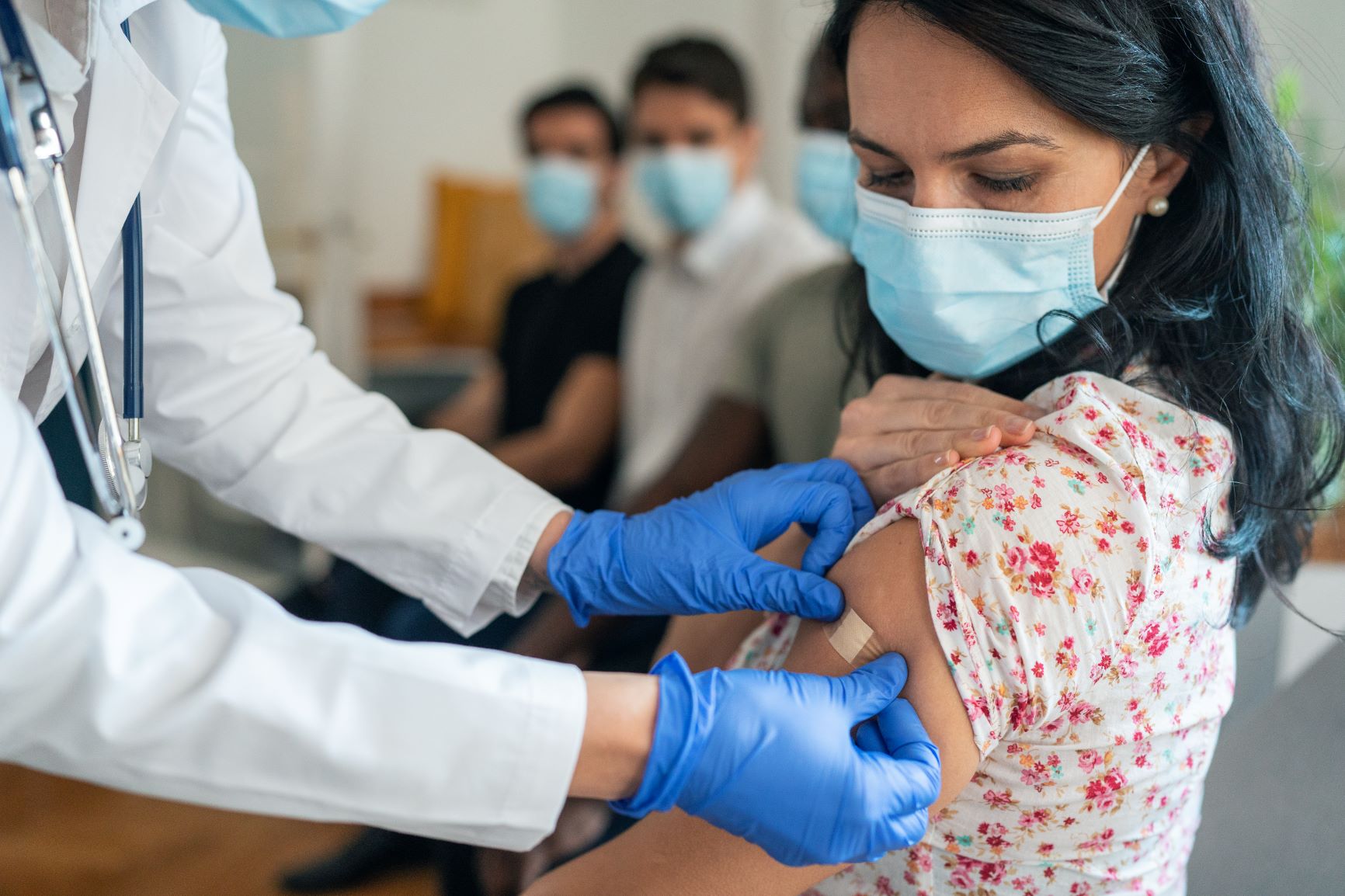 Pharmacist with blue gloves putting a band-aid on patient's arm after administering COVID treatment