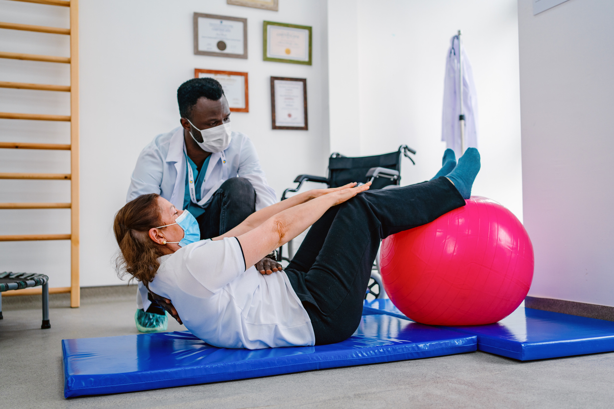 Physical therapist helping woman use a giant pink ball with chronic pain physical therapy