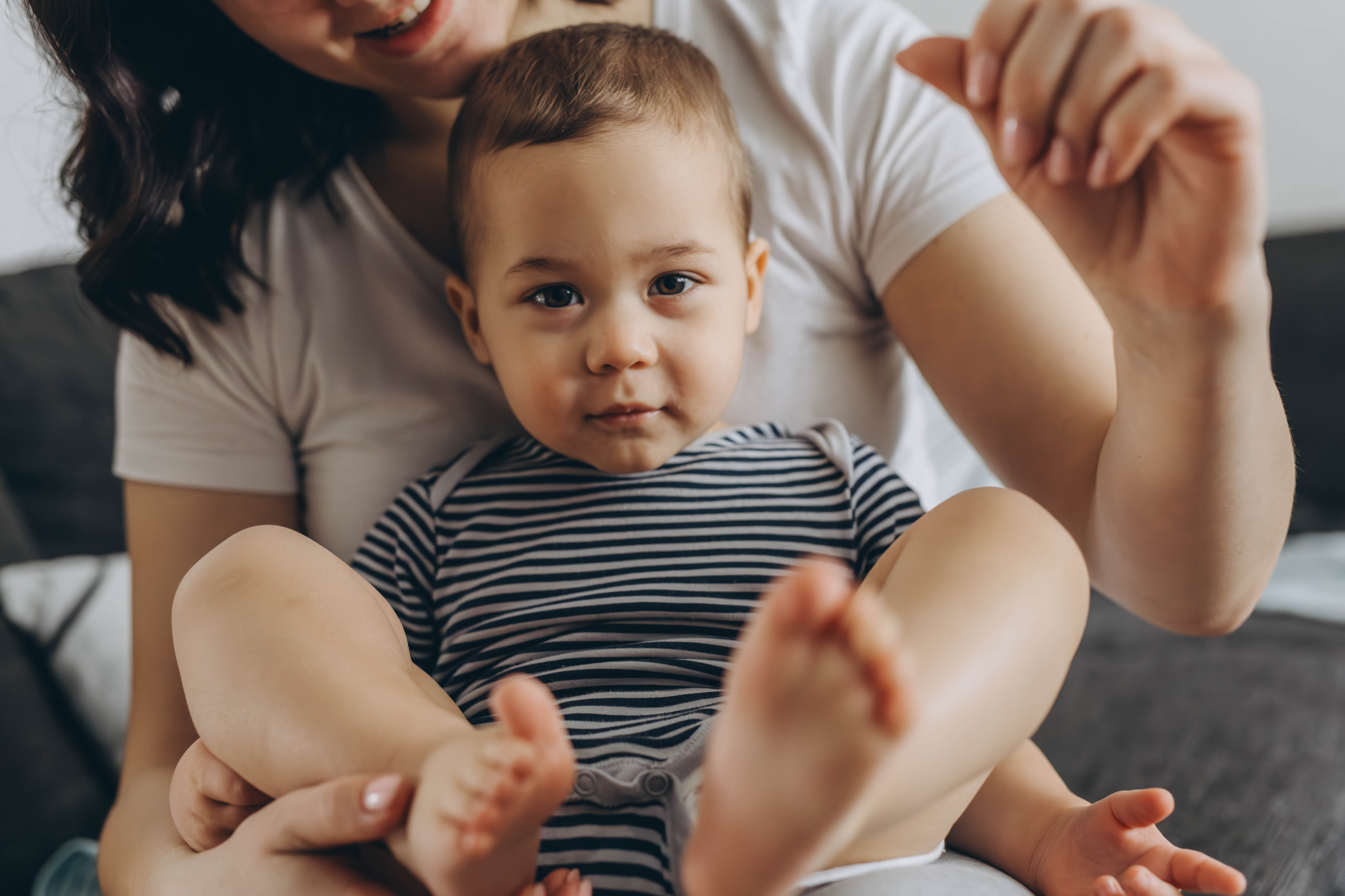 Two year old cute boy sitting in his mother arms, both smiling and enjoying a joyful moment together.