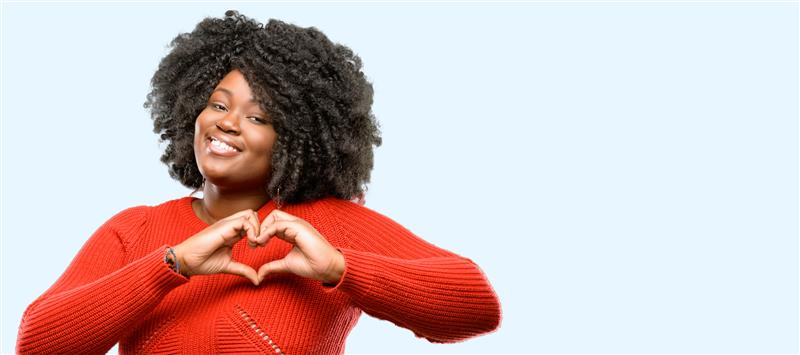 Smiling woman in a red sweater forms a heart with her hands, symbolizing care and heart health