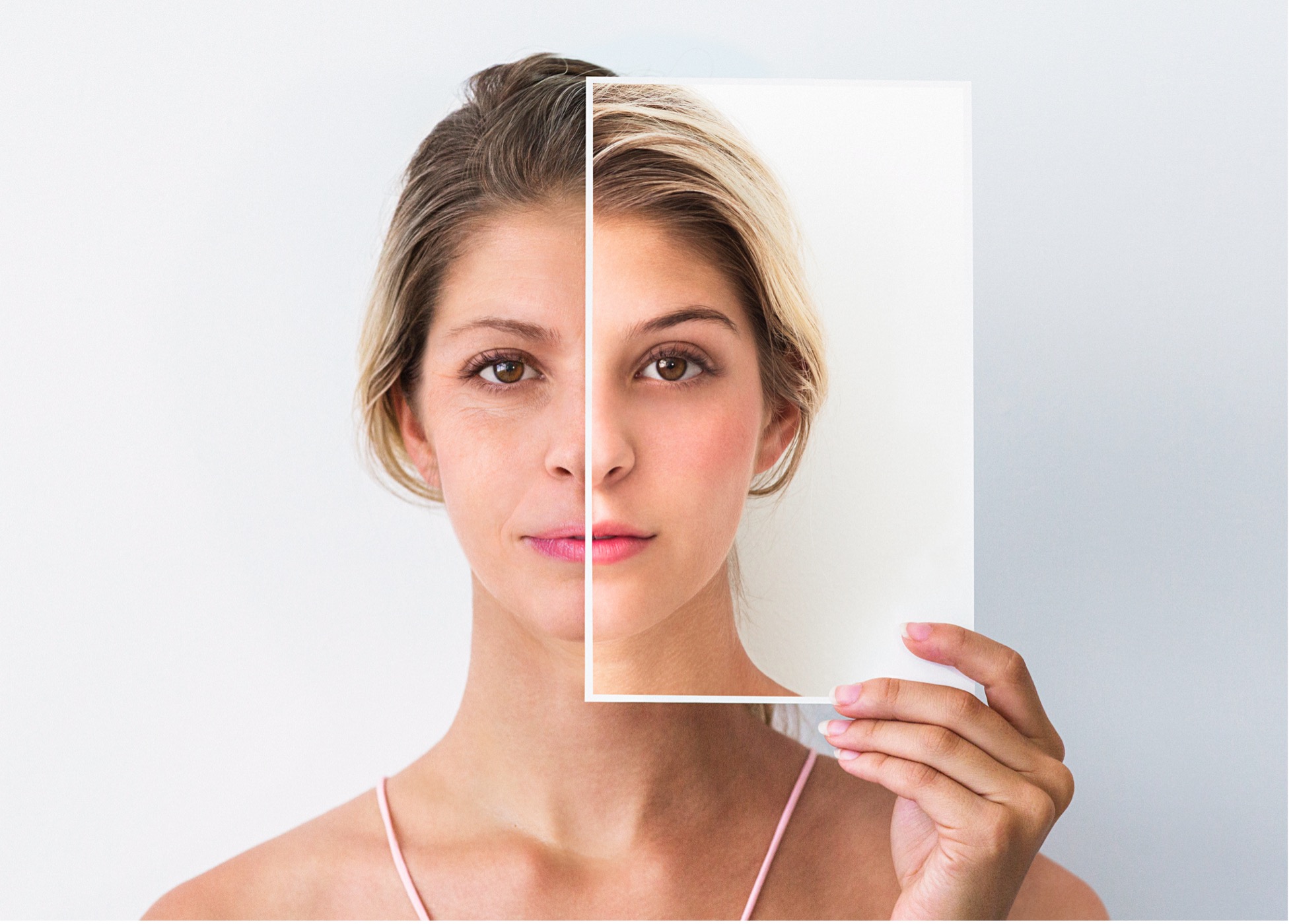Middle-aged woman holding photo of face when she was younger.Both people appearing in this image is the same person retouched to look old and young.