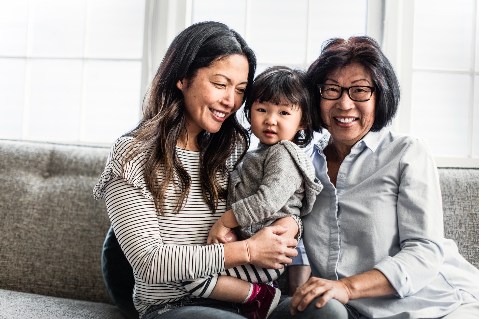 Mother and grandmother smiling while holding a young child on a couch, representing multigenerational women’s health and menopause care and support