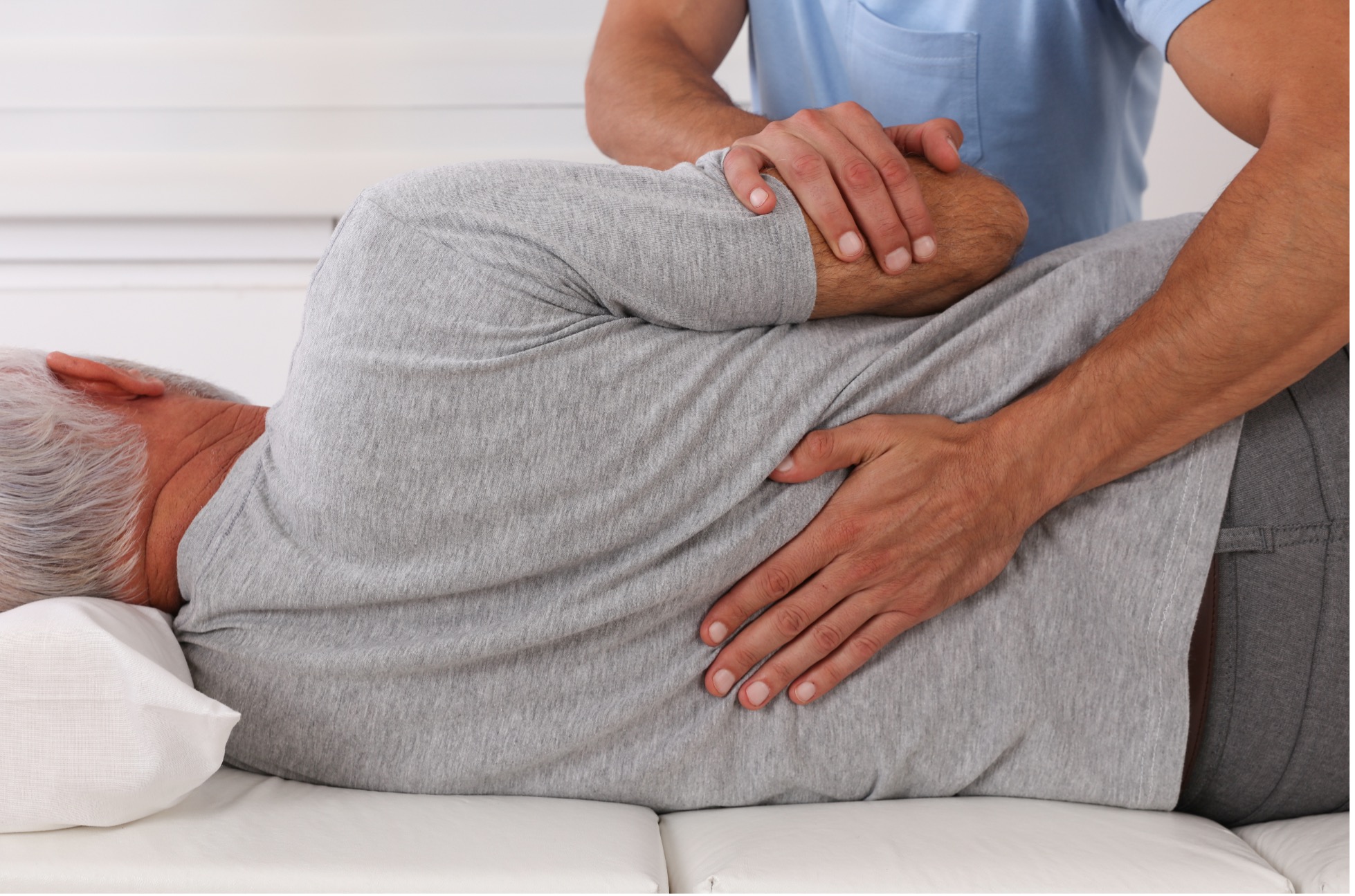 A chiropractor performs a spinal adjustment on an older adult lying on an examination table during a treatment session