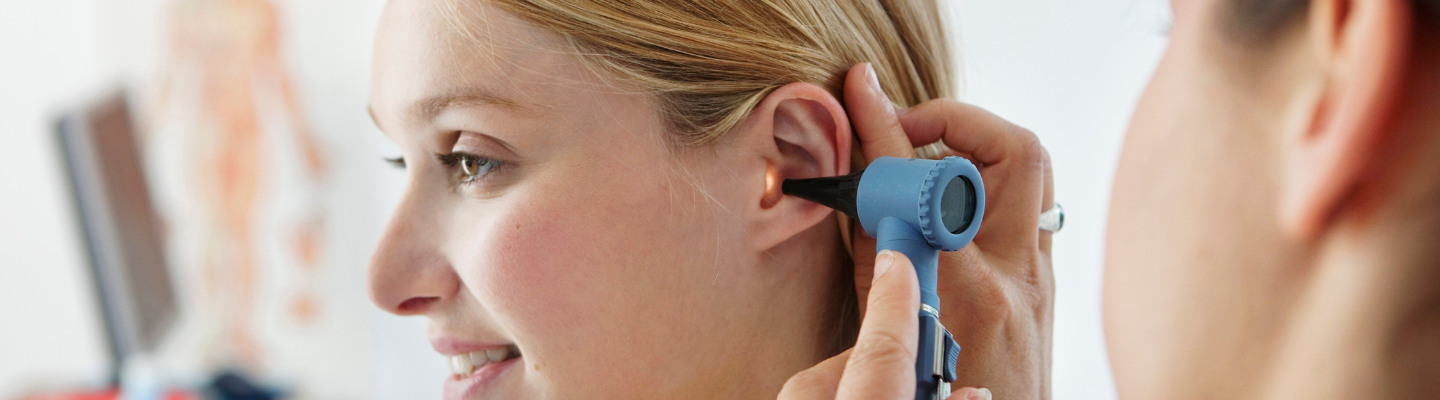 Woman at ear doctor having inner ear inspected with otoscope