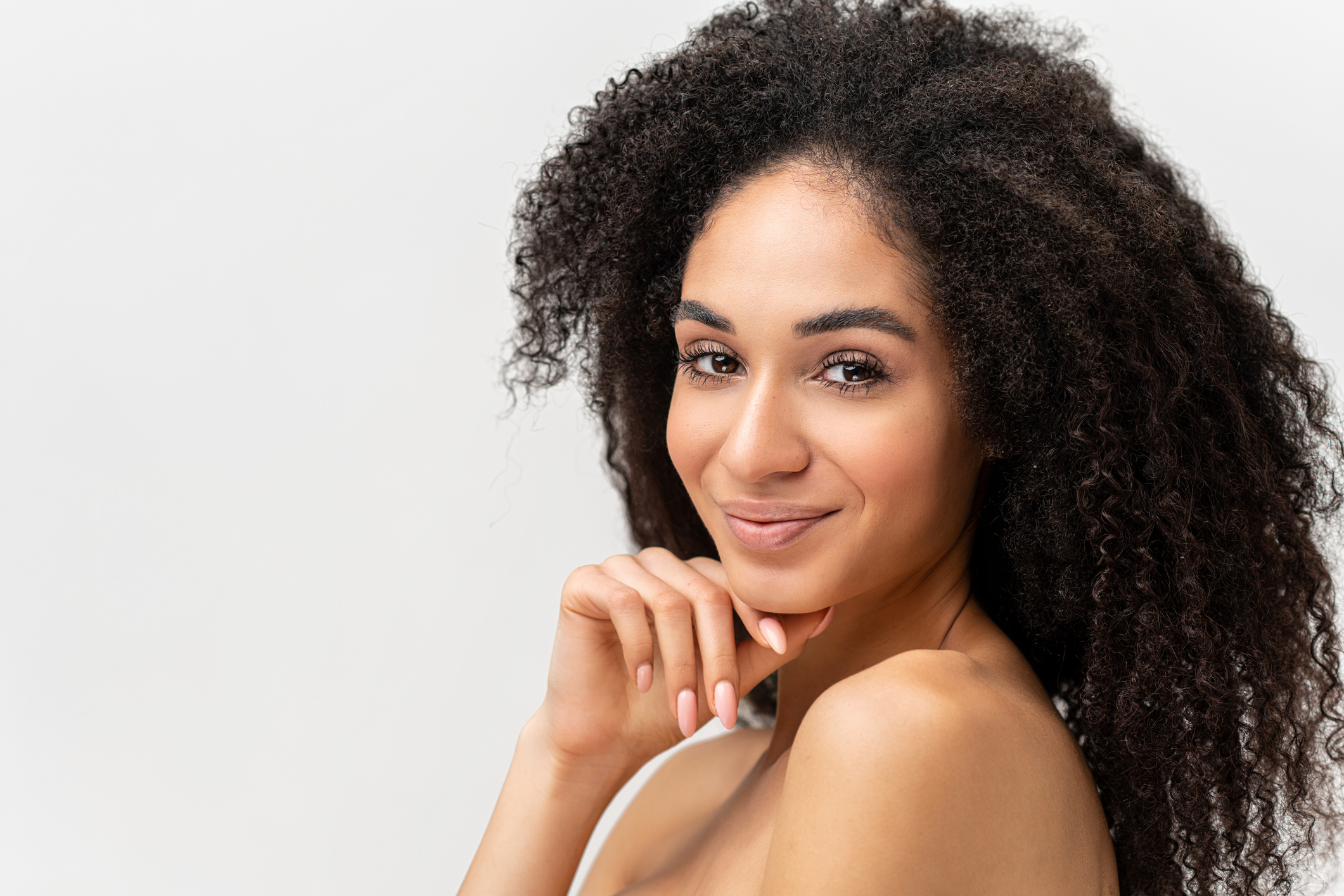 Fascinating attractive multiracial woman look at the camera over white background. Calm serene lady with naked shoulders gently touching face. Skin care concept