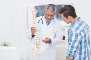 A doctor showing a patient how scoliosis is formed on a skeletal model