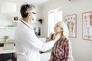 Doctor performing a physical exam on a woman to check for thyroid cancer around her jaw