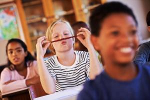 Young girl with ADHD with her classmates, balancing a pencil in between her nose and lips