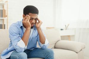 Young man in blue tightly gripping his head due to severe headache symptoms