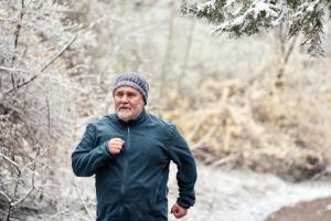 Elderly man in blue clothing running through snowy woods