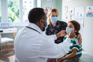 Doctor performing a pediatric ENT exam on a masked child