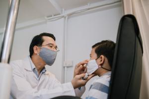 Masked doctor examining a young boy's eye for pink eye symptoms
