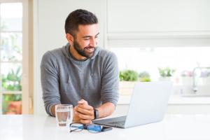Man sitting at his laptop with a glass of water practicing Dry January