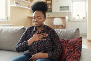 Woman sitting on couch gripping her chest after experiencing heartburn