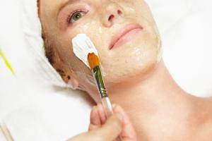 Attractive young woman gets a facial at a spa. She is wearing a white towel on her head. Vertical shot.