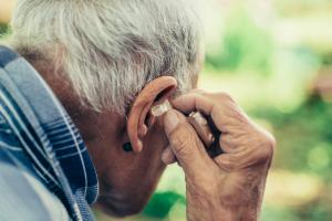 Older man adjusting hearing aid due to hearing loss and cognitive decline