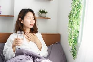 Woman with sore throat symptoms holding a glass of water
