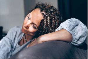 Portrait of a dreadlocks braid topknot bun woman sitting on the sofa. Concept of depression, loneliness, problems of adolescence