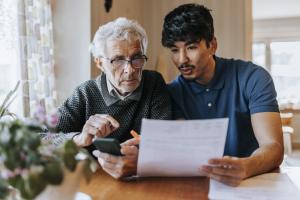Young man helping an elderly gentleman with paperwork and a cell phone