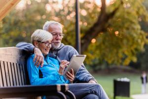 Smiling senior active couple sitting on the bench looking at tablet computer