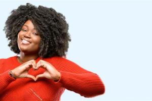 Smiling woman in a red sweater forms a heart with her hands, symbolizing care and heart health