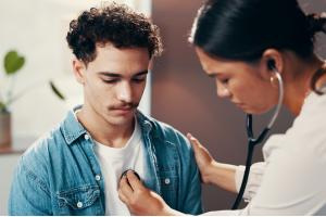 Doctor, patient and consultation for healthcare with stethoscope, chest exam or cardiology checkup. Medicine, health and people in hospital office for medical evaluation, listening to heart and help