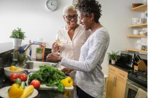 Two women smiling preparing fresh vegetables in the kitchen representing health lifestyle habits and support during menopause