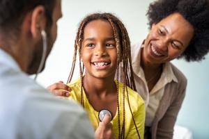 Smiling doctor examines a child with stethoscope in examination room.