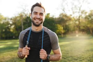 Handsome young strong sports man posing outdoors at the nature park location with skipping rope