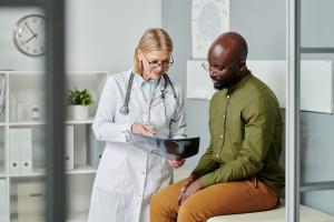 Confident mature doctor in whitecoat showing young black man x-ray image