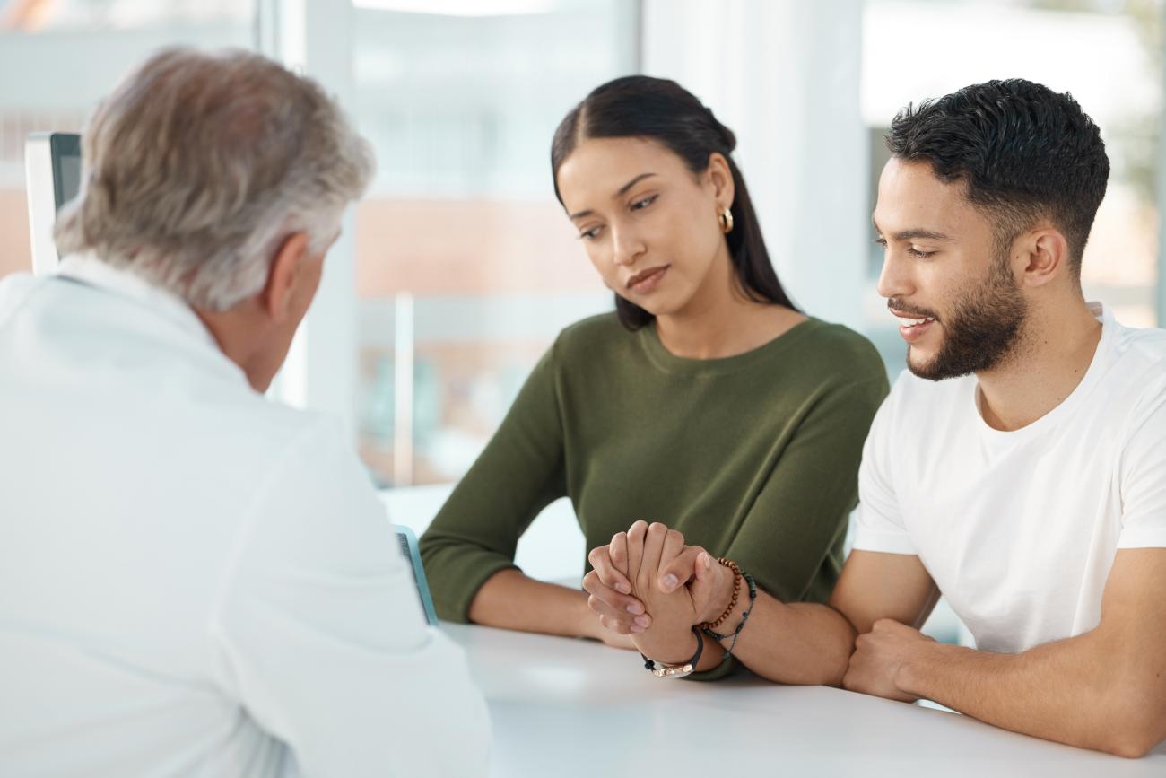  Shot of a young couple sitting with their genetic counselor and holding hands during a consultation