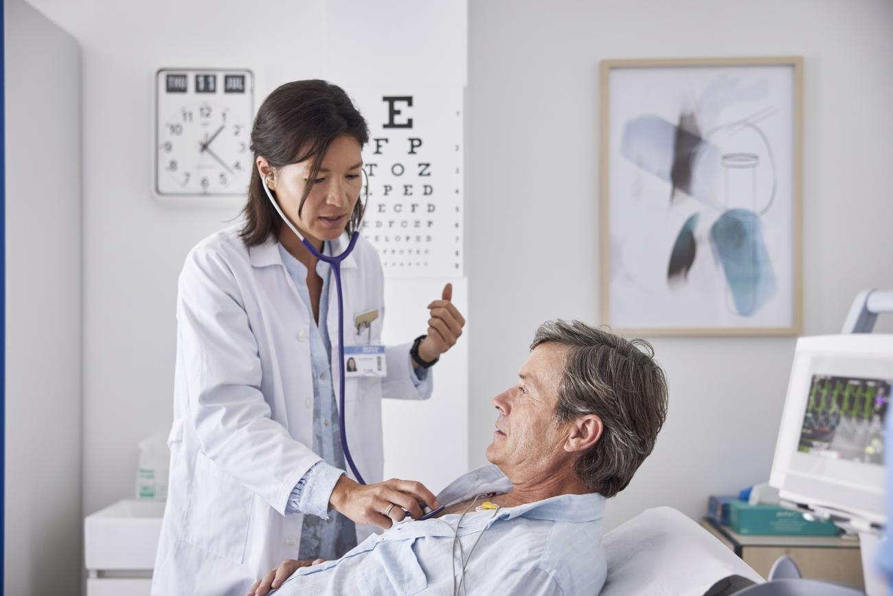 female doctor listening to male patient's heartbeat in an exam room