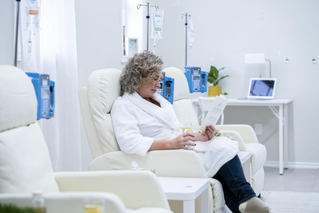 A middle aged woman sits in an oversized high back arm chair as she rests comfortably during her intravenous therapy treatment