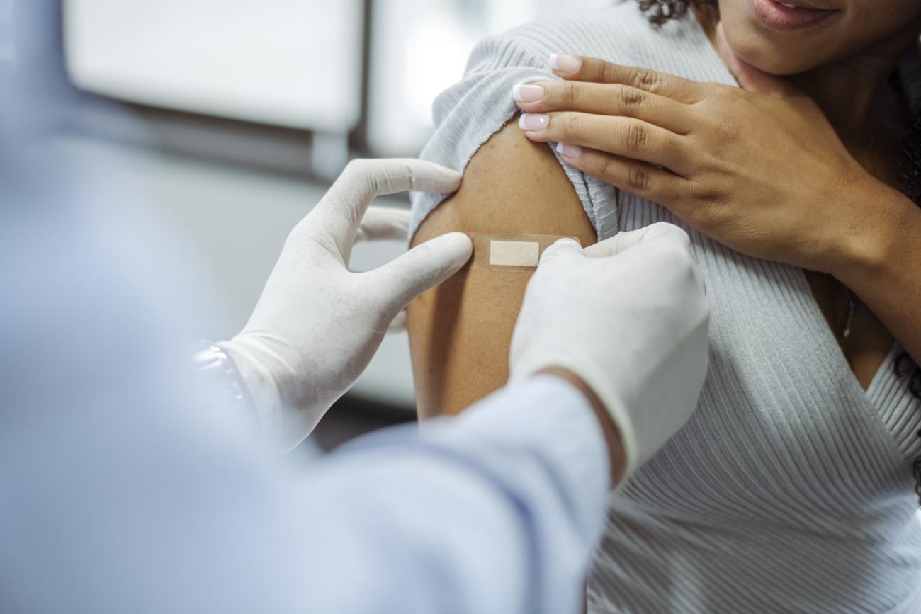 Close up shot of a doctor's hands applying a bandage on a female arm after patient received a vaccine